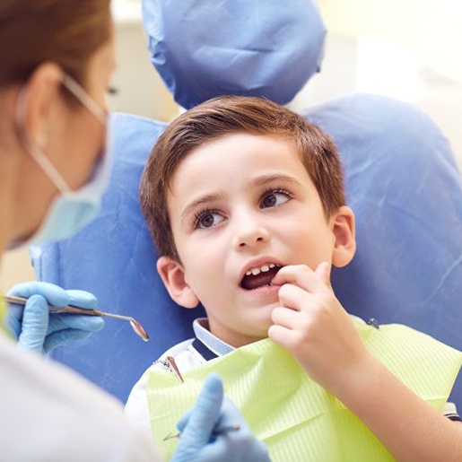 Young boy in dental treatment chair, pointing to his tooth