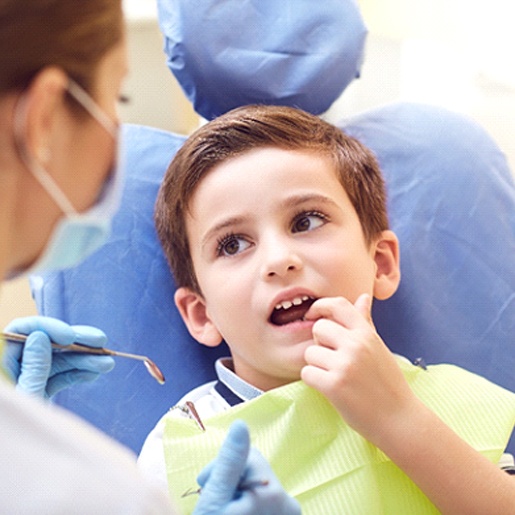 A young boy pointing to a bothersome tooth while a dentist prepares to check it