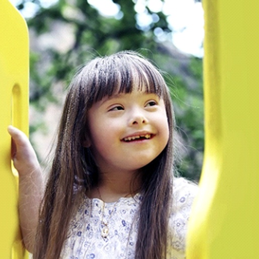 A young girl with special needs smiles while playing on a playground