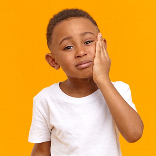 A young boy wearing a white t-shirt and holding his cheek in pain