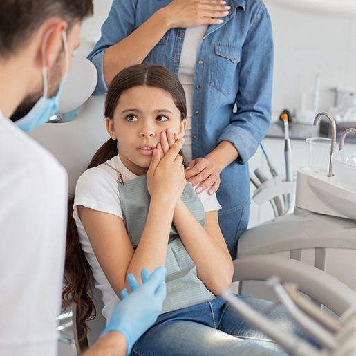 Girl with long hair and white shirt in dental chair holding her cheek in pain